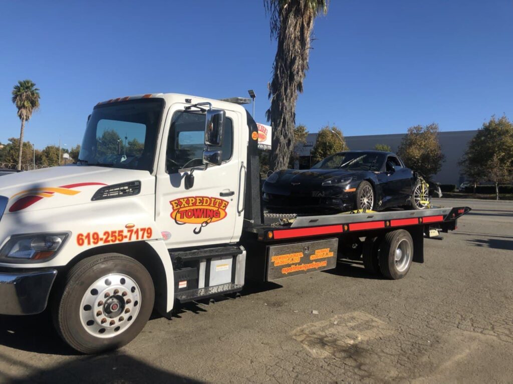 Expedite Towing flatbed tow truck towing a red car on a snowy road in San Diego.